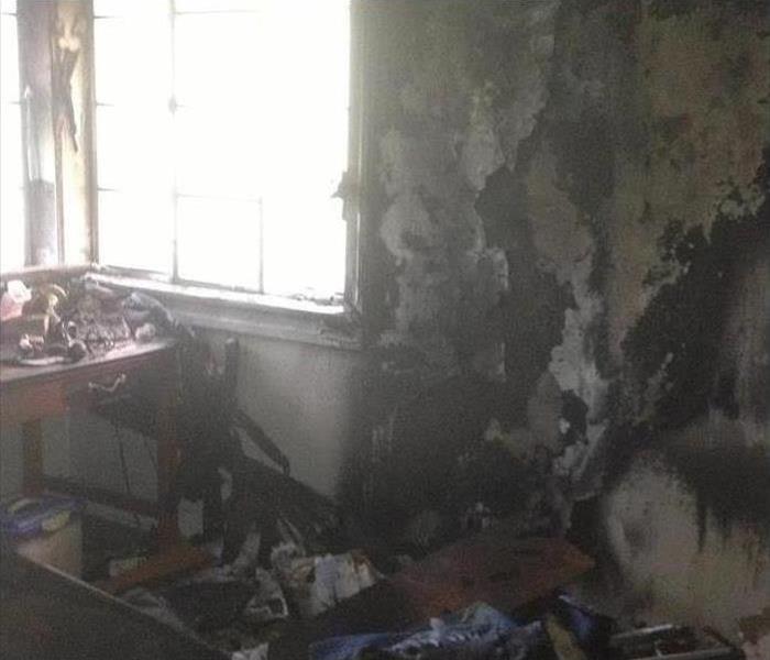 Burned walls inside a house, there is a window next to the wall the sunlight is shining. Burnt pieces on the floor